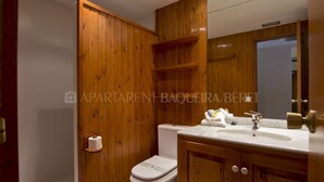 Un baño con paredes de madera, un inodoro blanco, un lavamanos con espejo y un perchero para toallas.