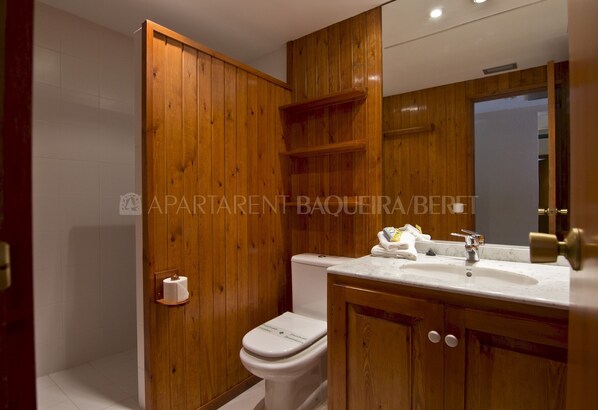 Ein Badezimmer mit Holzwänden, einer weißen Toilette, einem Waschbecken mit Spiegel und einem Handtuchhalter.