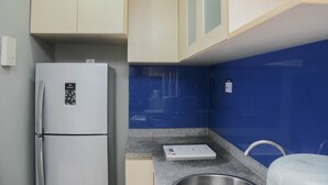 A compact kitchen with a white refrigerator, a built-in microwave, and a granite countertop. - Comfortable 2BR Apartment at Taman Melati Margonda (Depok)