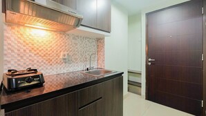 A kitchen with dark wooden cabinets, a stainless steel range hood, a tiled backsplash, and a built-in sink. - Simply Furnished Studio @ Grand Dhika City Apartment (Bekasi)