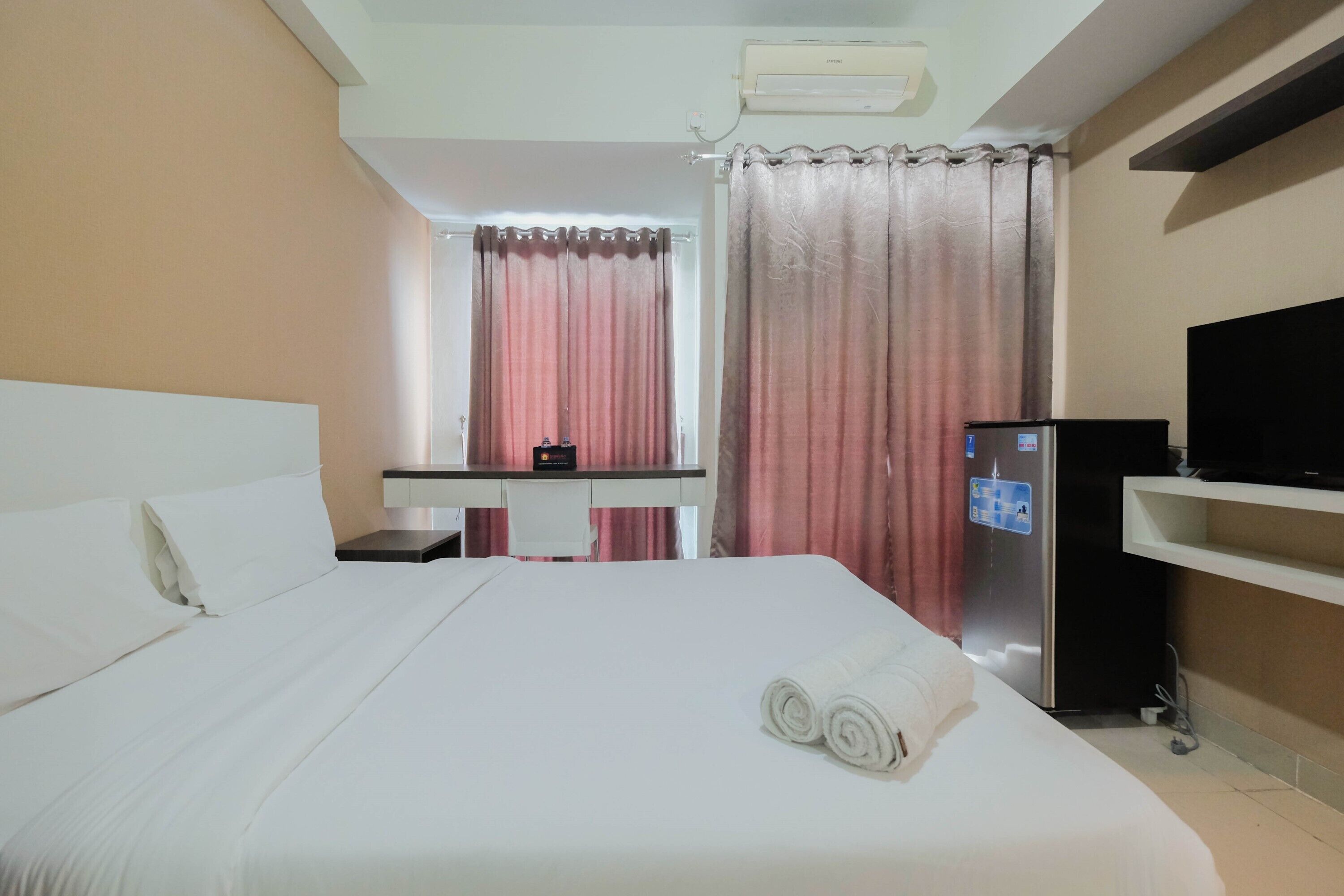 A hotel room with a bed, a desk, a television, and a refrigerator.