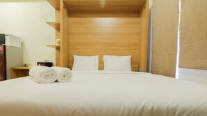 A hotel room with a wooden headboard, two white pillows, a neatly made bed, and a small bedside table with a lamp and a box. - Modern Studio Apartment 26th on Top of Green Pramuka Mall (Jakarta)
