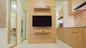 A modern kitchen with a flat-screen TV mounted on the wall, wooden cabinets, and a tiled floor. - Modern Studio Apartment 26th on Top of Green Pramuka Mall (Jakarta)