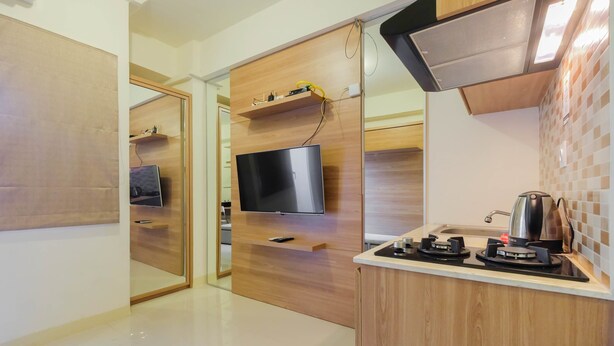 A modern kitchen with a built-in TV, wooden cabinets, and a gas stove. - Modern Studio Apartment 26th on Top of Green Pramuka Mall (Jakarta)