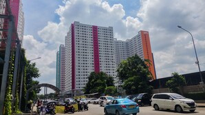 A multi-story building with a prominent pink stripe, surrounded by parked cars and greenery. - Modern Studio Apartment 27th on Top of Green Pramuka Mall (Jakarta)