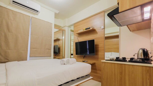 A hotel room with a bed, a TV, a kitchenette, and a mirror. - Modern Studio Apartment 27th on Top of Green Pramuka Mall (Jakarta)