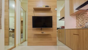 A modern kitchen with wooden cabinets, a built-in TV, and a tiled backsplash. - Modern Studio Apartment 27th on Top of Green Pramuka Mall (Jakarta)