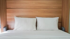 Een bed met witte lakens en twee kussens, tegen een houten hoofdbord.