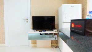 Quarto com televisão de tela plana em suporte branco, frigorífico branco da LG e uma mala travelio sobre uma bancada.