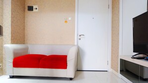 Um sofá branco com um cobertor vermelho, uma porta fechada e uma televisão em um suporte.