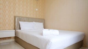 Cama bem arrumada com lençóis e almofadas brancos, uma mesinha de cabeceira e parede estampada.
