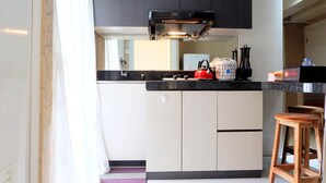 Uma cozinha compacta com bancada preta, armários brancos, chaleira vermelha e um banquinho de madeira.