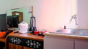 A kitchen with a microwave, coffee maker, and utensils on the counter, a sink, and a mirror reflecting the room. - Simply Studio Apartment at Green Pramuka City (Jakarta)