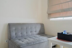 Ein graues, gepolstertes Sofa vor einer Wand mit einem Fenster darüber.