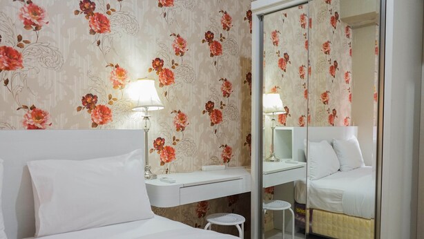 Ein Hotelzimmer mit Bett, Nachttisch, Spiegel, einem kleinen Hocker und einem Badezimmer mit Toilette und Waschbecken.