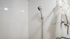 Ein Duschbereich mit weißen Fliesen, einer Handbrause und einem weißen Duschvorhang mit Muster.