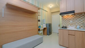 A compact kitchen with wooden cabinets, a built-in bench, a refrigerator, and a gas stove. - New Modern Studio Apartment at Green Pramuka City (Jakarta)