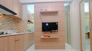 A modern kitchen with wooden cabinets, a tiled backsplash, and a flat-screen TV mounted on the wall. - New Modern Studio Apartment at Green Pramuka City (Jakarta)