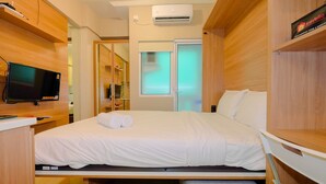 A compact hotel room with a bed, a television, and a wardrobe. - New Modern Studio Apartment at Green Pramuka City (Jakarta)