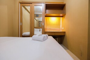 Une chambre d’hôtel avec un lit, une armoire en bois, un bureau avec une lampe et une salle de bain visible à travers une porte.
