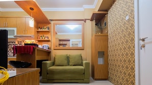 Een ruimtelijk ingerichte leefruimte met kitchenette, een groene bank, een wand met behangpapier en een houten kast.