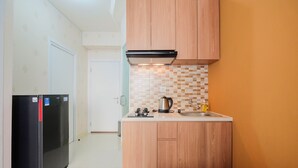 A compact kitchen with wooden cabinets, a built-in oven, and a tiled backsplash. - 2BR Apartment Green Pramuka City near Shopping Mall (Jakarta)
