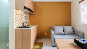 A compact kitchen with wooden cabinets, a tiled backsplash, and a grey sofa in a living area. - 2BR Apartment Green Pramuka City near Shopping Mall (Jakarta)