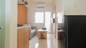 A compact kitchen with a refrigerator, a wooden table, and a sofa. - 2BR Apartment Green Pramuka City near Shopping Mall (Jakarta)