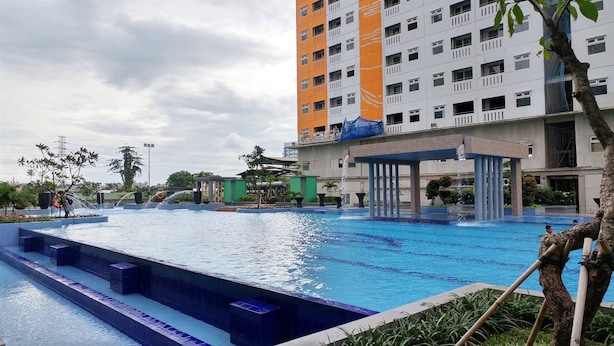 A swimming pool with a water fountain, surrounded by greenery and a multi-story building with balconies. - 2BR with Mall Access at Green Pramuka Apartment (Jakarta)