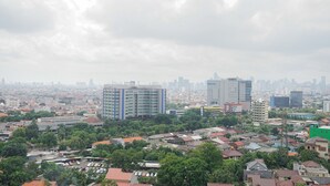 A cityscape with a mix of residential and commercial buildings, including a prominent multi-story building with a blue and white facade. - Cozy Studio Green Pramuka Apartment next to Mall (Jakarta)