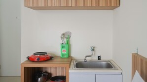 A compact kitchen with a wooden cabinet, a red induction cooktop, a sink, and a green utensil holder. - Cozy Studio Green Pramuka Apartment next to Mall (Jakarta)
