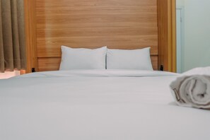 Ein ordentlich gemachtes Bett mit weißen Leinen und Kissen, ein hölzernes Kopfteil und ein zusammengerolltes Handtuch auf dem Bett.
