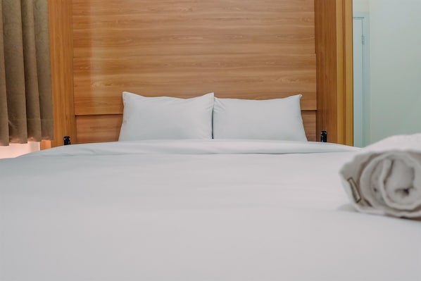 A neatly made bed with white linens and pillows, a wooden headboard, and a rolled towel on the bed.