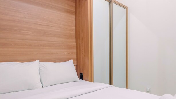 A neatly made bed with white linens in a modern room with wooden paneling and a sliding glass door closet. - Connected to Mall 2BR Apartment at Green Pramuka City (Jakarta)