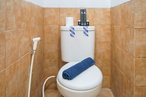 A bathroom with a white toilet, a blue towel on the seat, and a toilet paper holder on the tank.