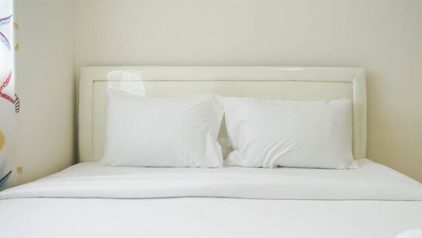A bed with white bedding and pillows, a plain headboard, and a wall with a curtain featuring a colorful pattern.