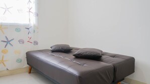 A modern, dark brown sofa with wooden legs in a room with a tiled floor and a wall decorated with starfish and seashells.