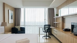 A modern hotel room with a large bed, a desk, a chair, a television, and a window with curtains. - Studio Apartment with Mall Access at U Residence (Curug)