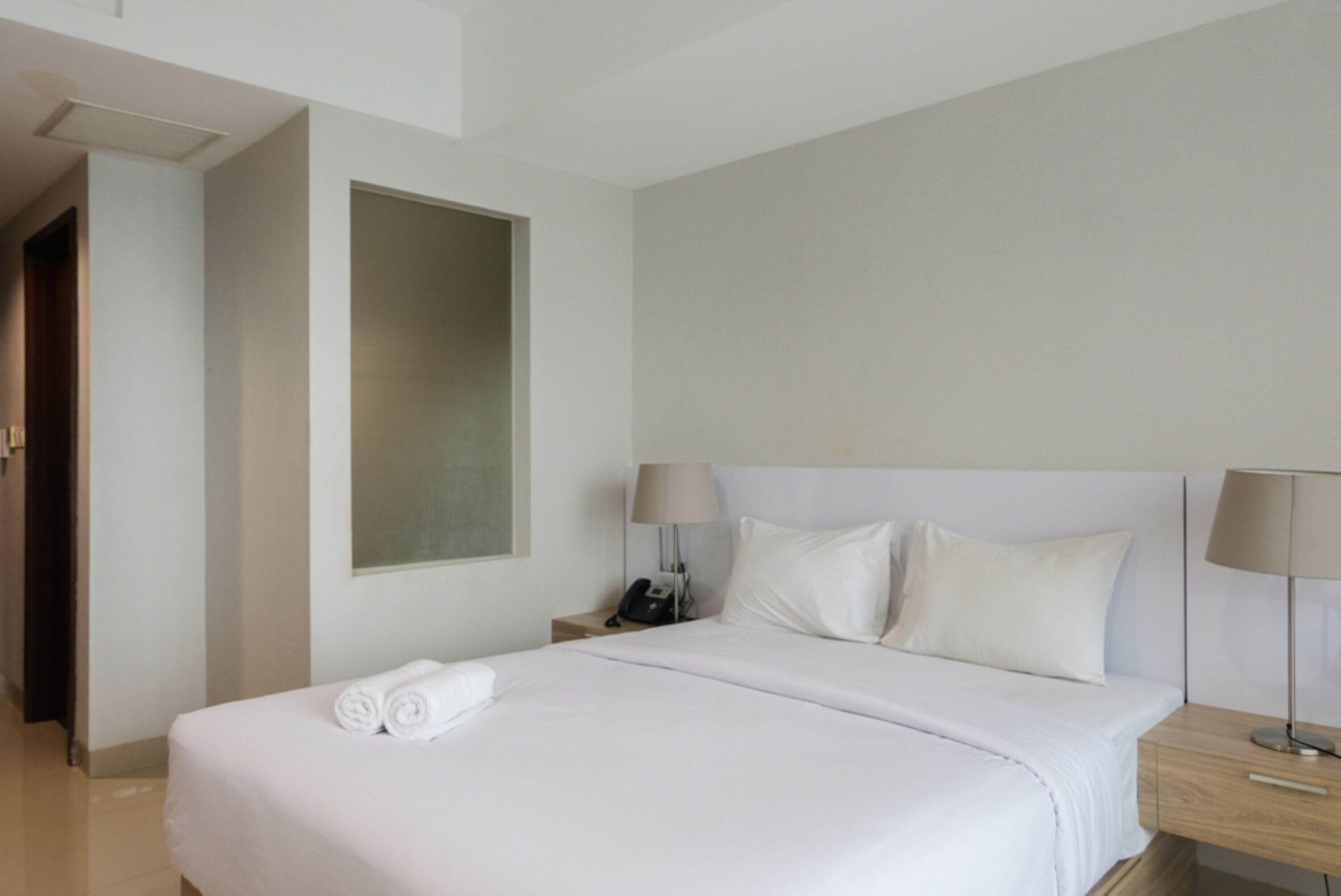 A hotel room with a neatly made bed, a bedside table with a lamp, and a phone.