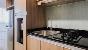 A kitchen with a stainless steel sink, a gas stove, wooden cabinets, and a built-in microwave. - Studio Apartment with Mall Access at U Residence (Curug)
