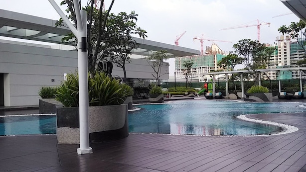 A modern outdoor swimming pool with a wooden deck, surrounded by planters and a covered seating area. - Studio Apartment with Mall Access at U Residence (Curug)