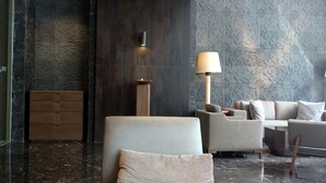 A modern lobby with a marble floor, a wooden cabinet, a tall floor lamp, and a sofa set. - Classy Studio Apartment at U Residence (Curug)