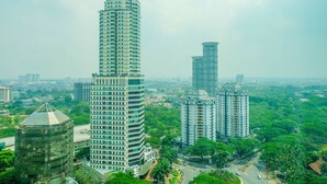 A high-rise building with a cylindrical shape and a pointed top, surrounded by other tall buildings and lush greenery. - Classy Studio Apartment at U Residence (Curug)