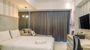 A modern hotel room with a large bed, a desk, a chair, a TV, and a large window with curtains. - Classy Studio Apartment at U Residence (Curug)
