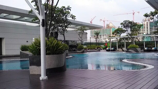 A modern outdoor pool area with a wooden deck, surrounded by planters and a covered seating area. - Classy Studio Apartment at U Residence (Curug)