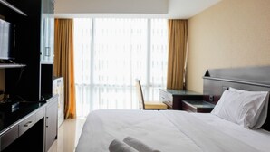Ein Hotelzimmer mit Bett, Schreibtisch, Fernseher und Blick auf ein Gebäude durch große Fenster.