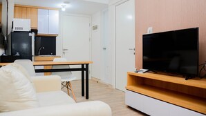 A modern living room with a flat-screen TV, a sofa, a dining table, and a kitchen area with a refrigerator and microwave. - Cozy 2BR at Springlake Summarecon Bekasi Apartment (Bekasi)