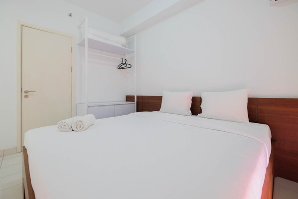 A neatly made bed with white linens and two pillows, a wooden headboard, and a white wardrobe with a hanging rack.