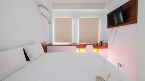 Een hotelkamer met een bed, een bureau, een aan de muur bevestigde televisie en een raam met jaloezieën.