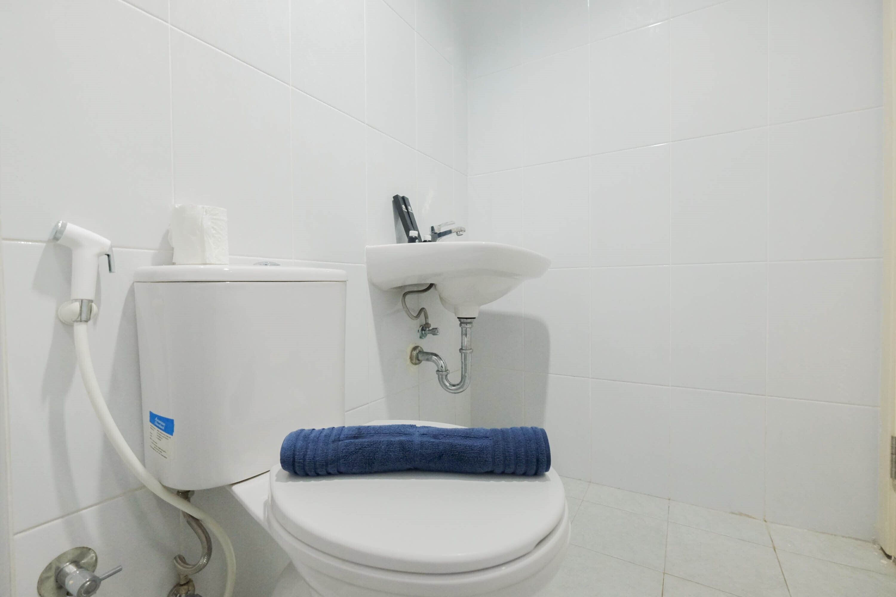 Une salle de bain avec des toilettes blanches, un lavabo et une serviette bleue posée sur la lunette des toilettes.